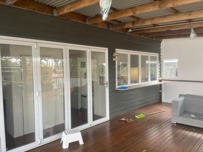 Outdoor deck with dark gray siding, white doors/window, and wooden floor. A small stool is present.