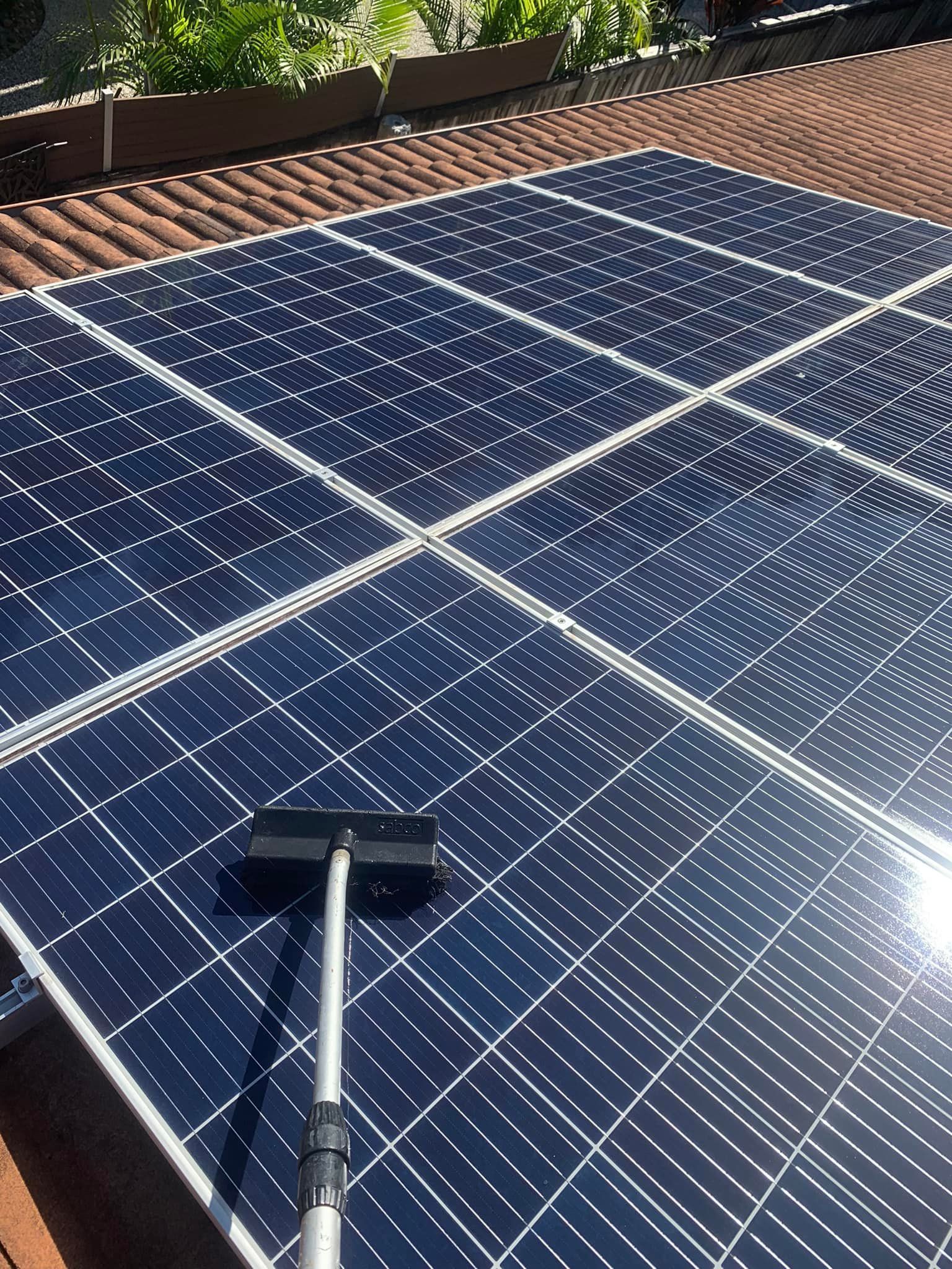 Solar panels on a roof being cleaned with a long handled brush; sunny day.