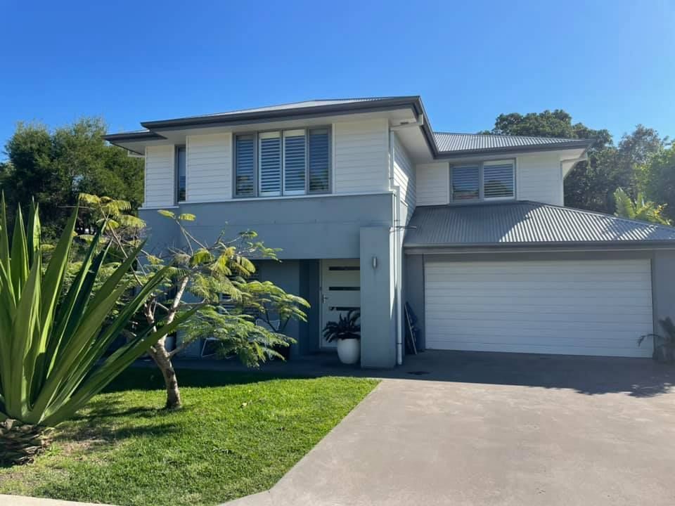 Two-story house with gray and white exterior, a garage, and a driveway, under a clear blue sky.