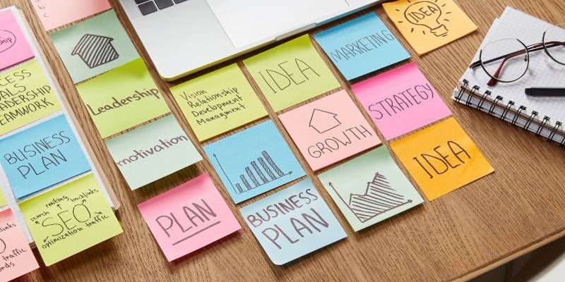 A desk with sticky notes on it and a laptop.