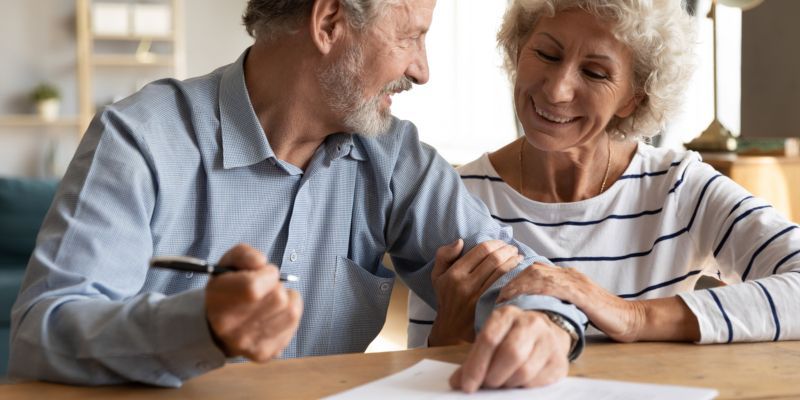 An elderly couple is sitting at a table signing a document.