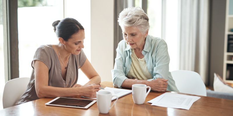 Two women are sitting at a table looking at a tablet.