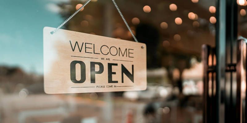 A welcome open sign is hanging on a glass door.