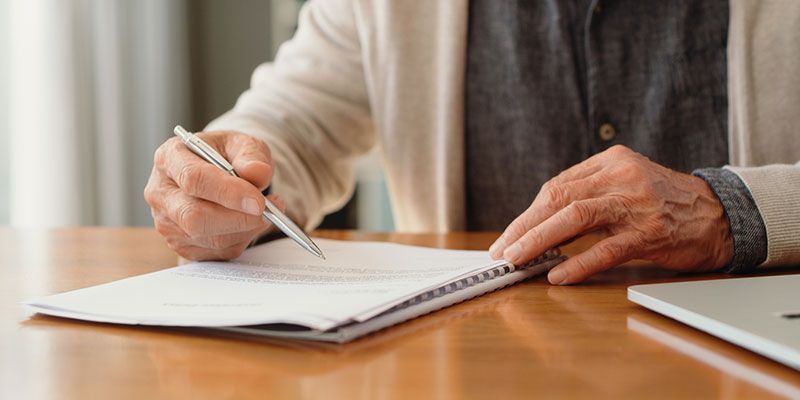 A man is sitting at a table writing in a notebook with a pen.