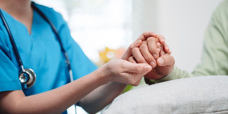 A nurse is holding the hand of an elderly woman.