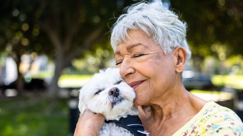 An elderly woman is holding a small white dog in her arms.