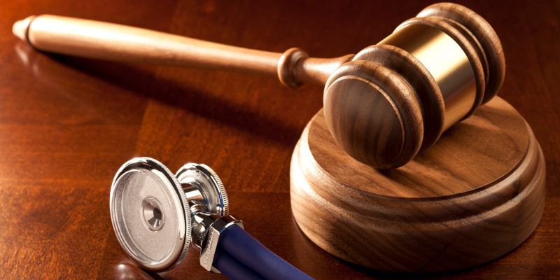 A stethoscope sits next to a wooden gavel on a wooden table