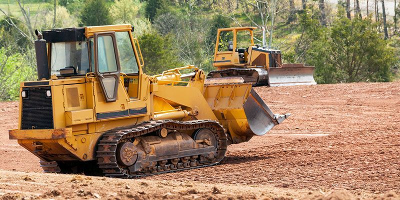 Two bulldozers are working on a dirt field.