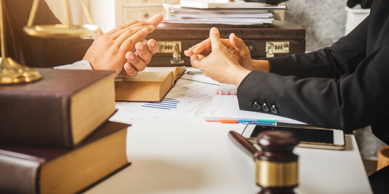 Two lawyers are sitting at a table with a gavel and books.