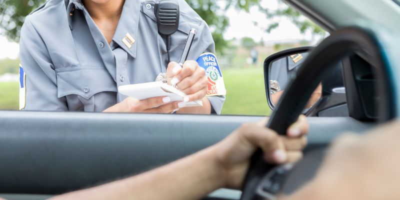 A police officer is writing a ticket to a driver in a car.