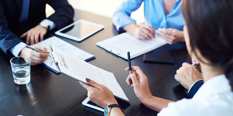 A group of people are sitting around a table with papers and a tablet.