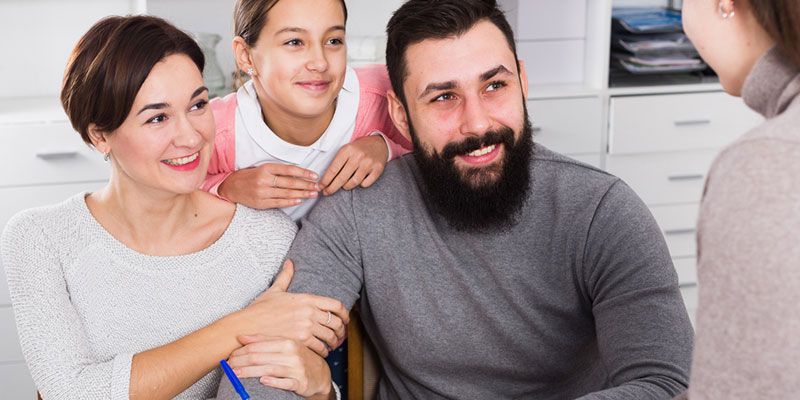 A family is sitting at a table talking to a woman.