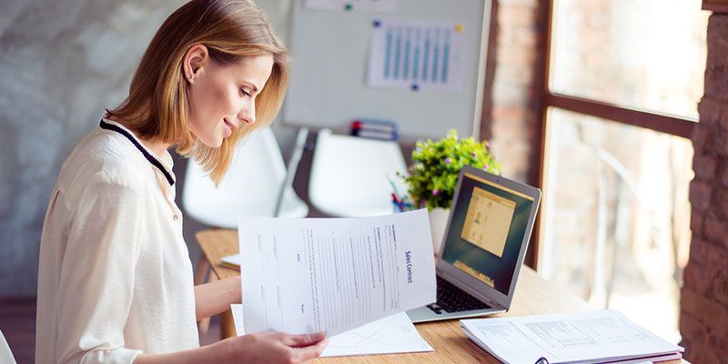 A woman is sitting at a desk with papers and a laptop.