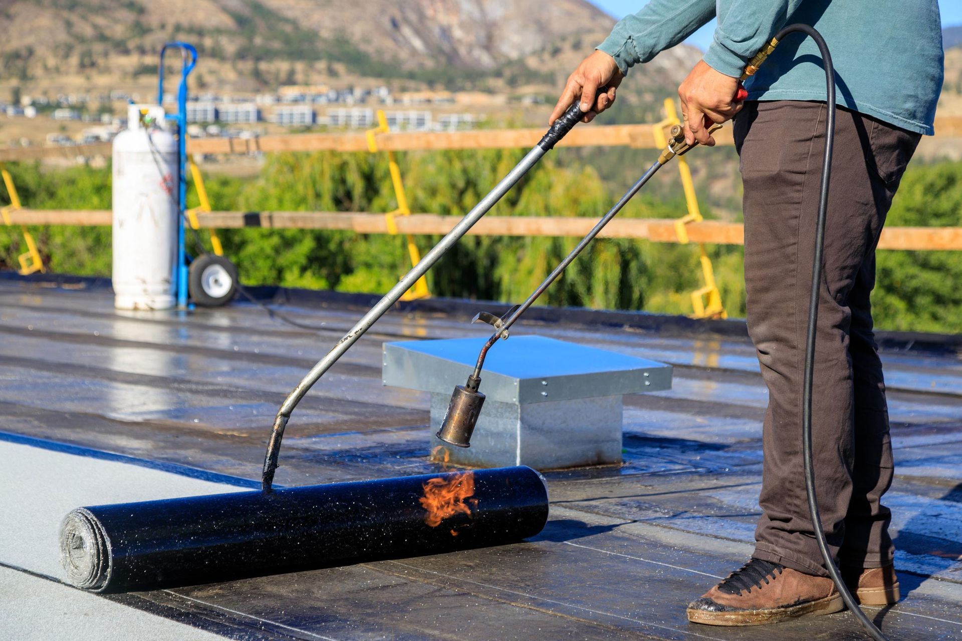 A roofer torches a membrane layer on a flat roof. A roofer torches a membrane layer on a flat roof.