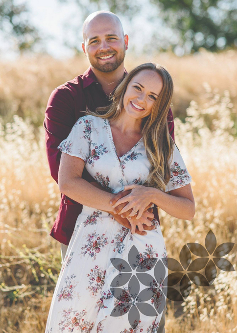 Couple embracing in a sunlit field, smiling among tall dry grass.