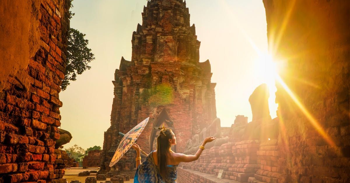 Woman with parasol poses near ancient temple ruins, bathed in golden sunlight.