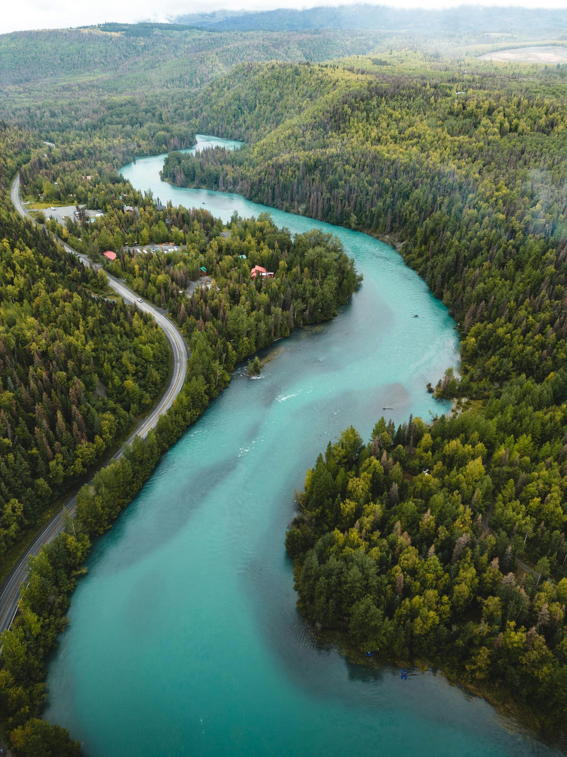 Turquoise river winding through lush green forest, with a road alongside.