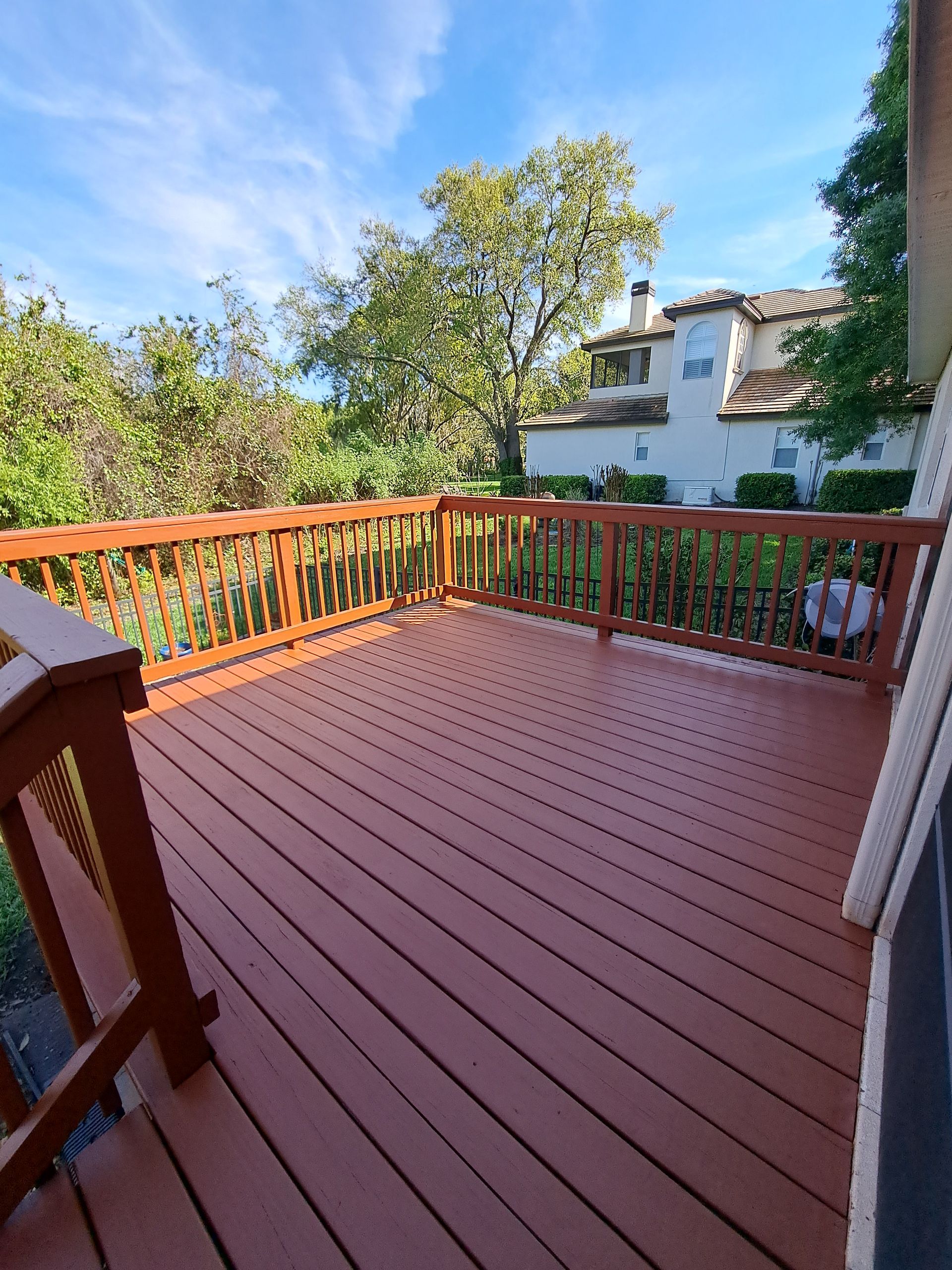 Wooden deck overlooking trees and a building with a blue sky.