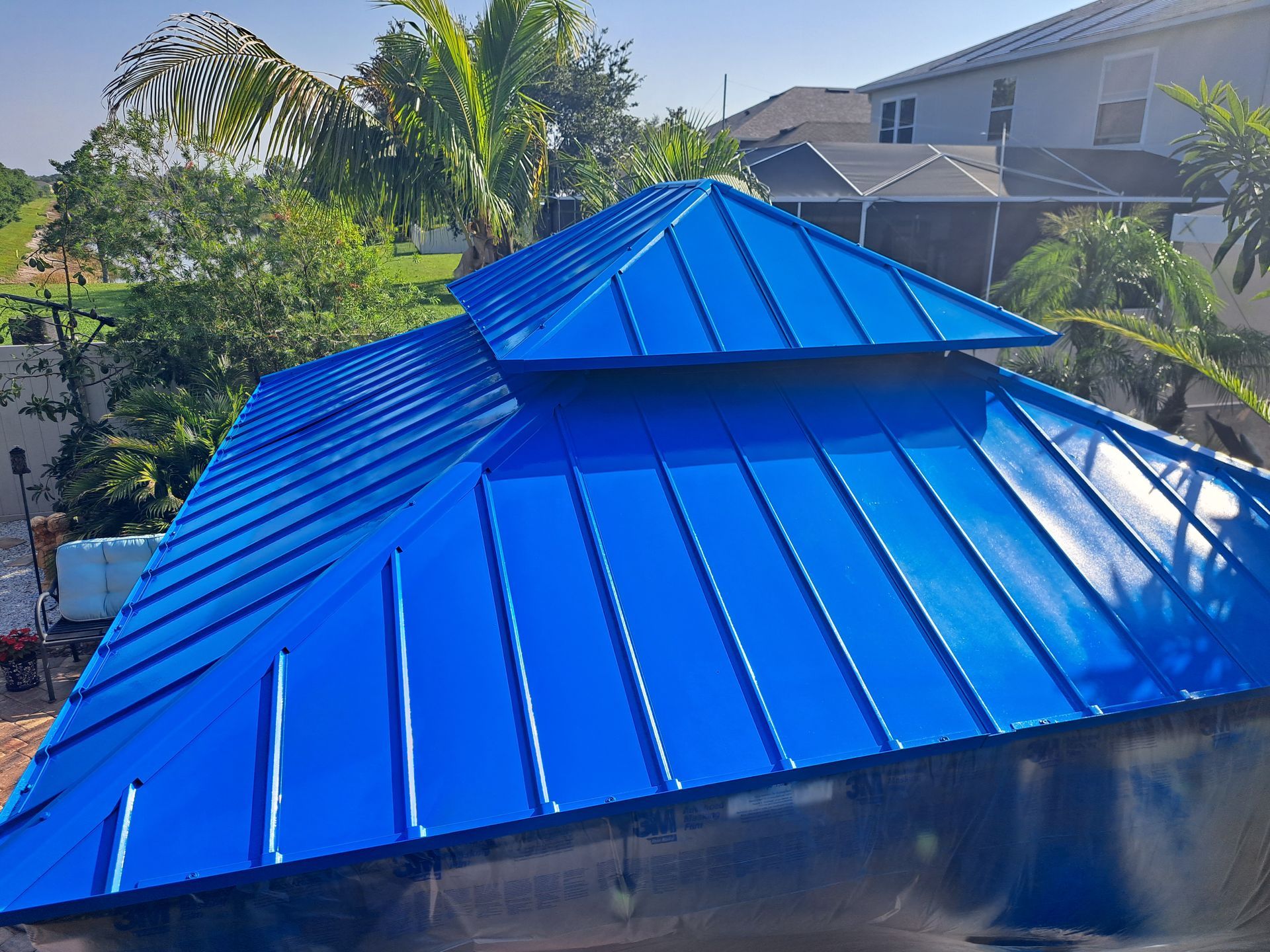 Blue metal roof of a gazebo, with a multi-tiered design, in a sunny outdoor setting.