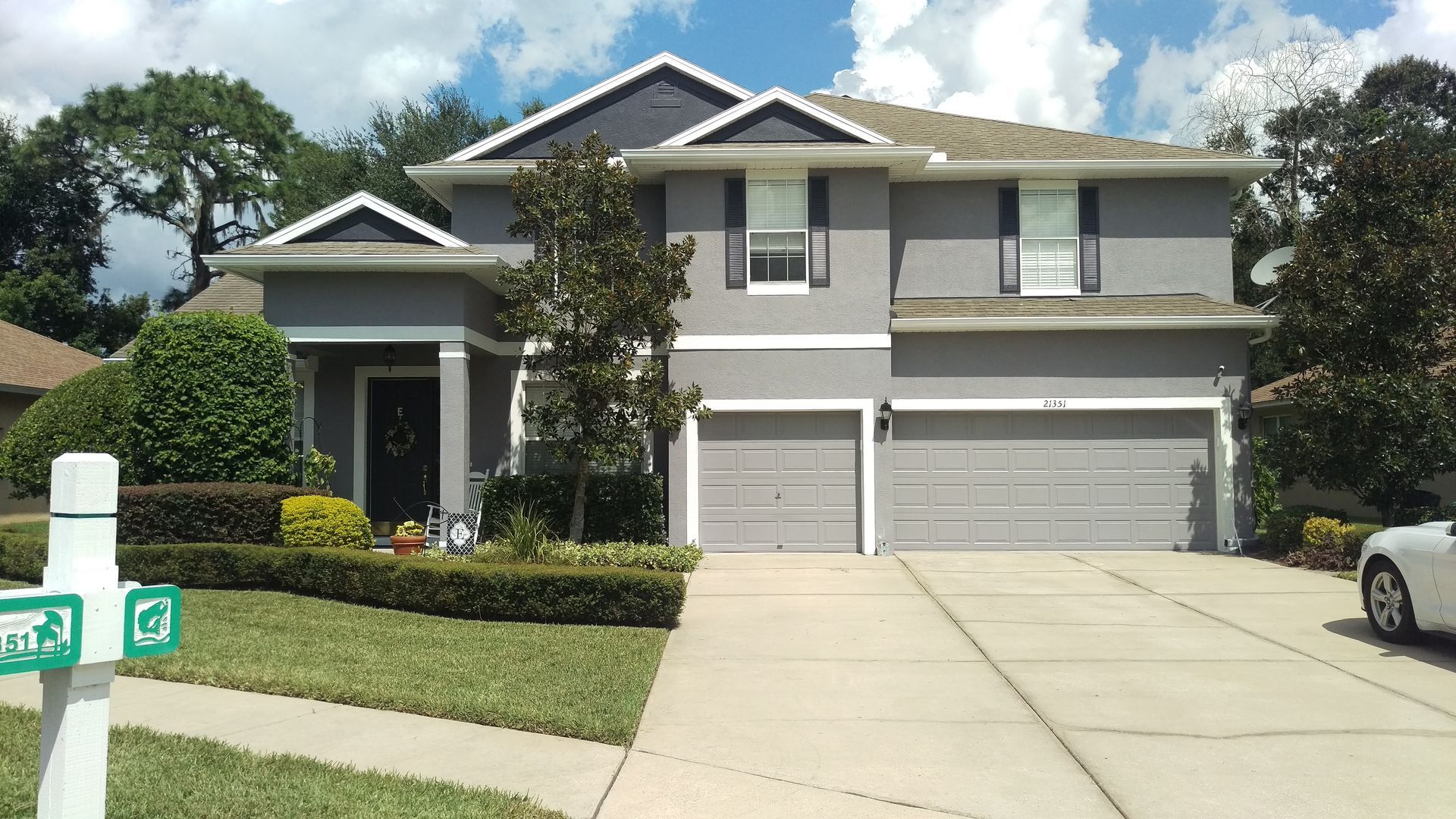 Gray two-story house with a driveway, lawn, and trimmed bushes on a sunny day.