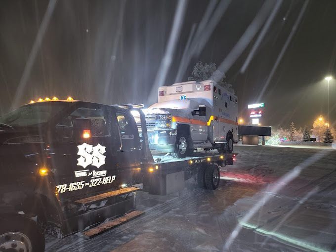 Tow truck hauling a white vehicle through heavy snow at night on a wet road