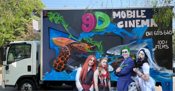 A group of people are standing in front of a mobile cinema truck.