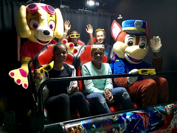 A group of children are riding a roller coaster with mascots.