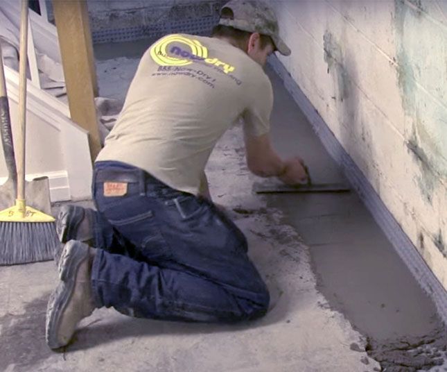 Worker kneels applying wet concrete along a wall in a construction area