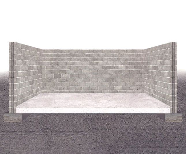 Empty brick stall with a concrete floor and low walls on a gravel surface.