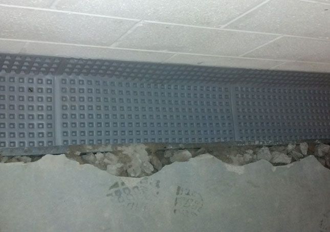 Damaged wall beneath a blue perforated panel and white ceiling tiles