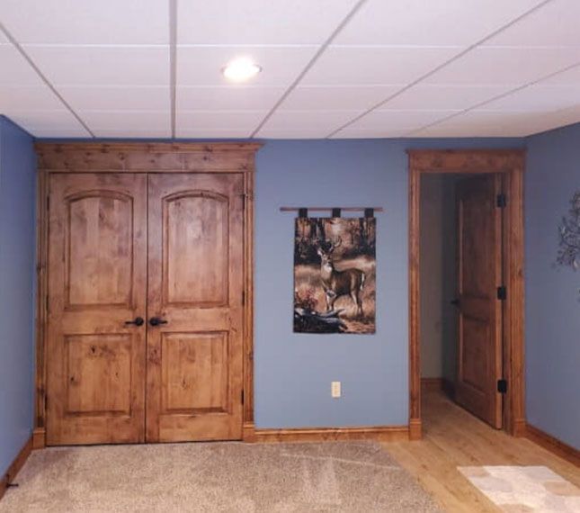 Basement room with blue walls, wood trim, two wooden doors, and a wall painting above carpet and tile flooring
