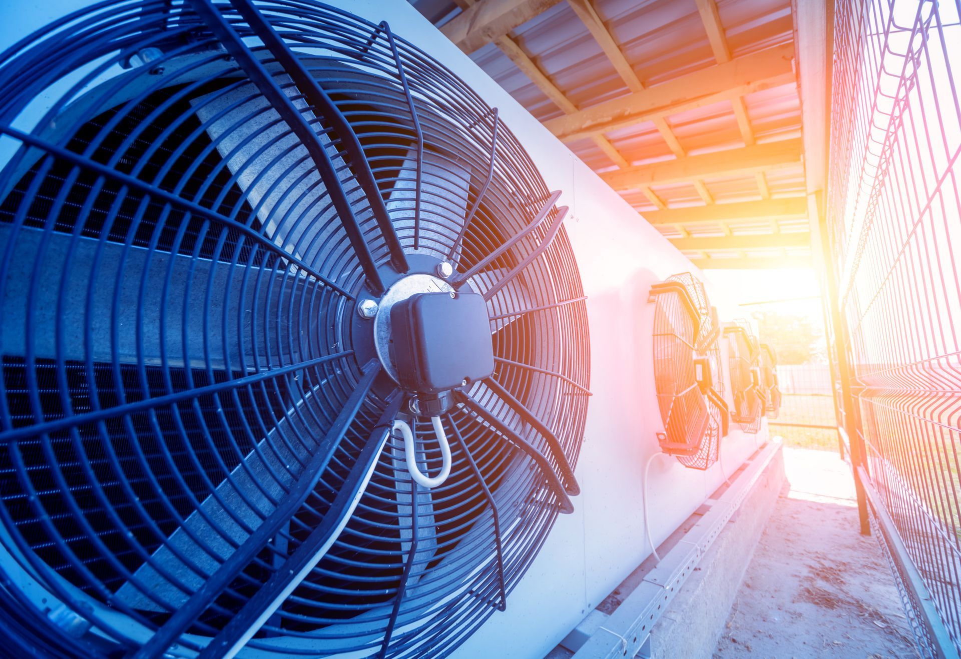 Large industrial air conditioning units outdoors, with fan blades and bright sunlight.
