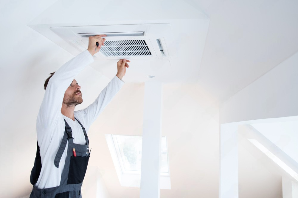 Person installing an air conditioning vent in a white ceiling.