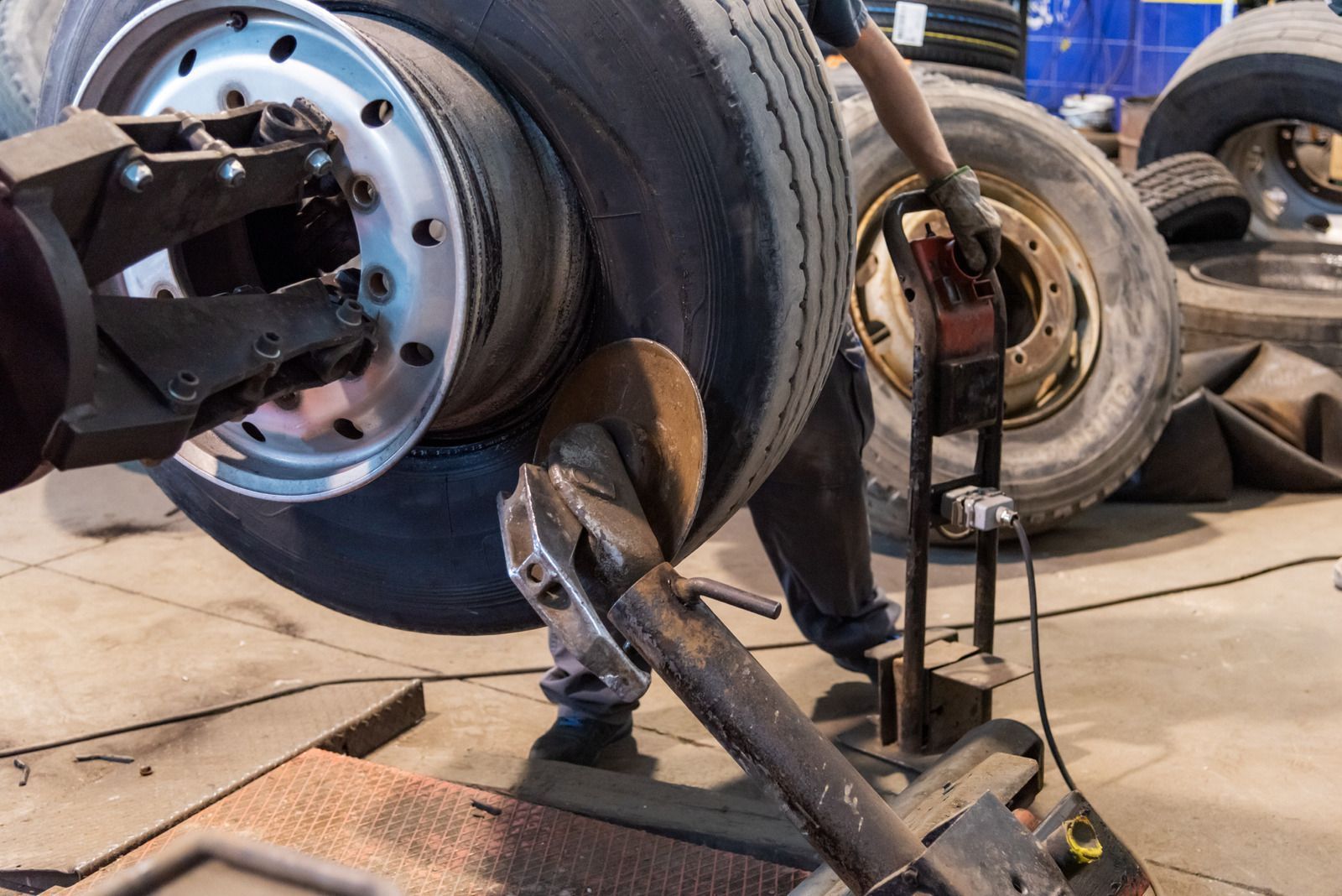 A worker uses a heavy-duty mechanical tool to remove a large tire from a metal rim in a workshop.