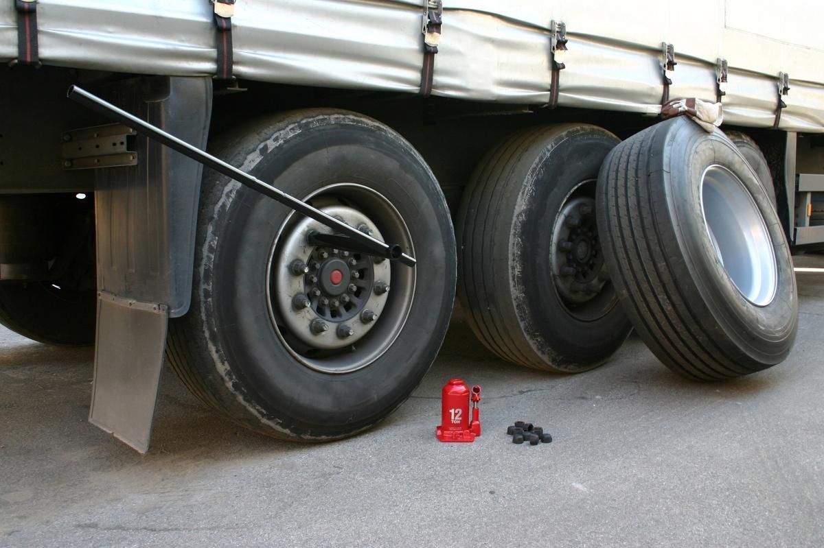 Truck tire being changed; spare tire and jack near the wheels. Black wrench in use.