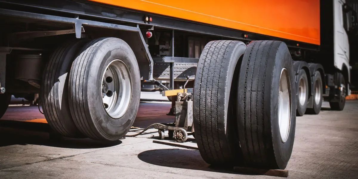 Close-up of semi truck wheels and tires under an orange trailer in a parking lot