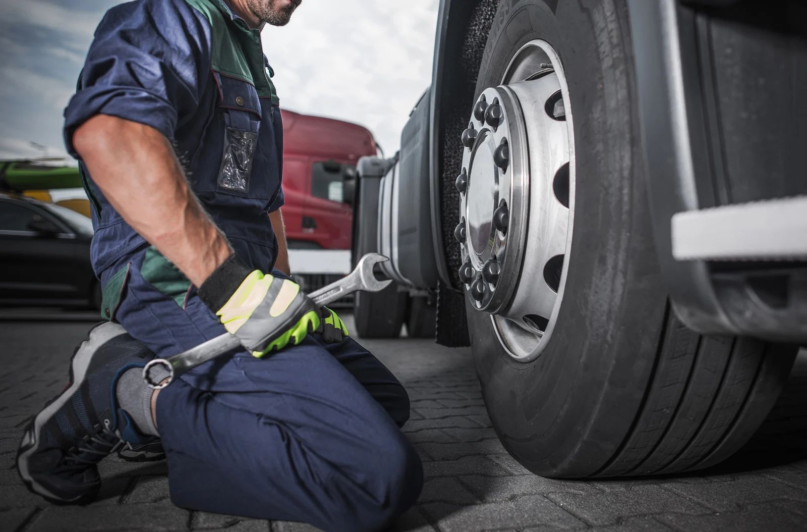 Mechanic kneeling beside a truck wheel, using a wrench on the lug nuts.