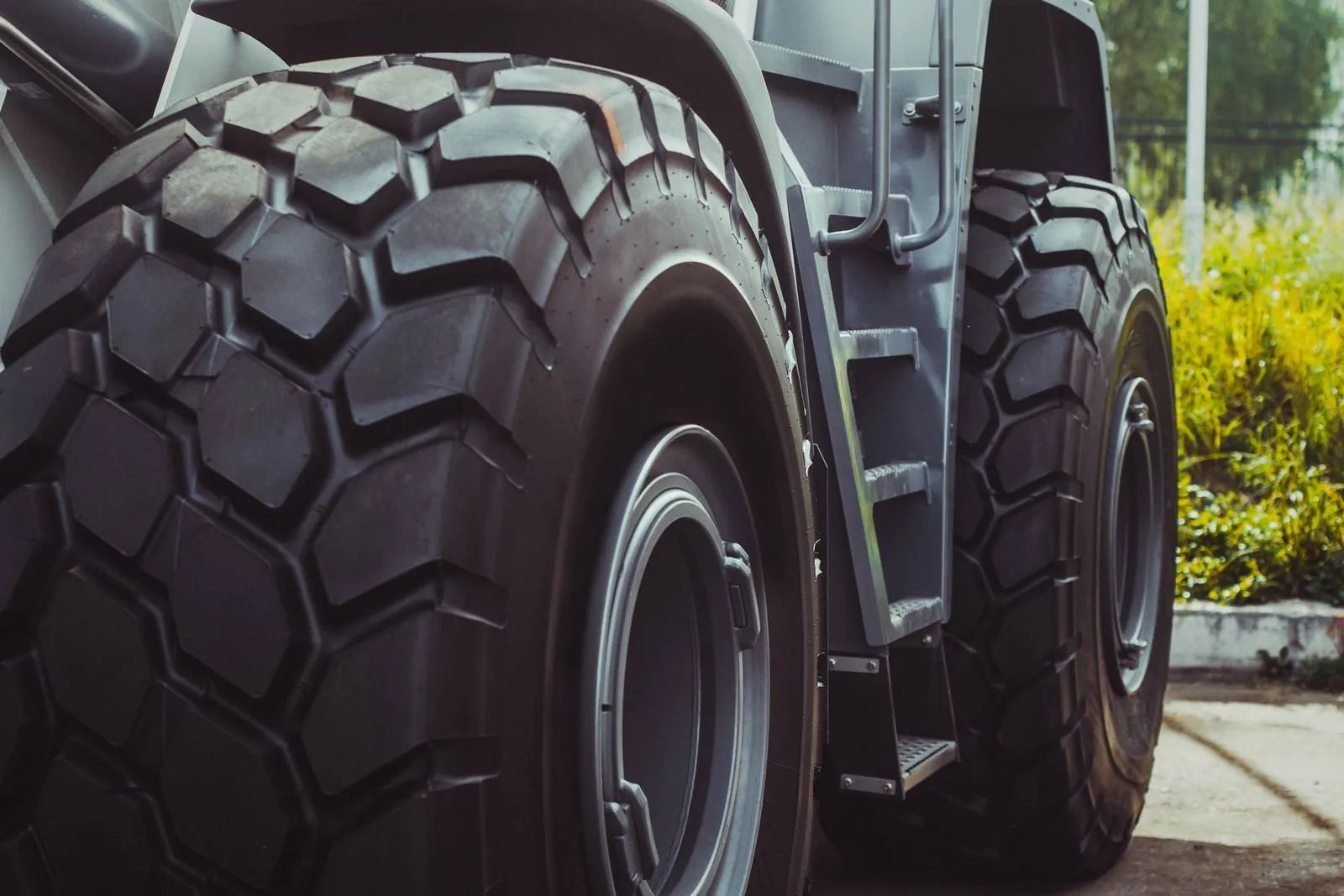 Close-up of large, black, treaded tires on a gray construction vehicle parked outside on a sunny day.
