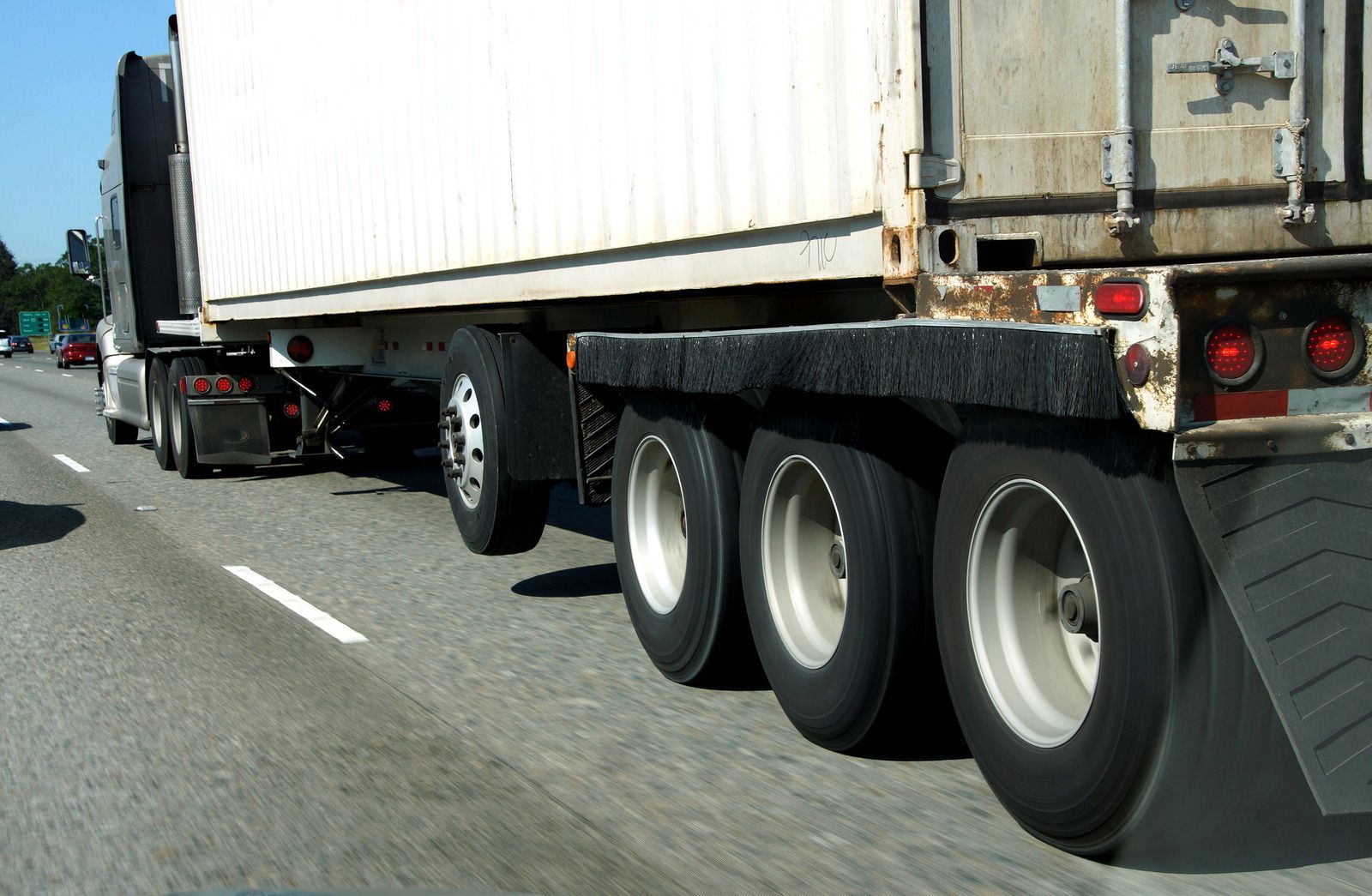 Semi truck trailer with three rear axles driving on a highway.