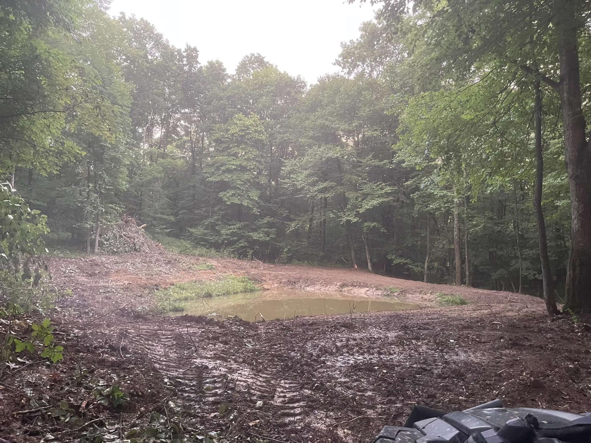 A motorcycle is parked in the middle of a muddy field in the woods.