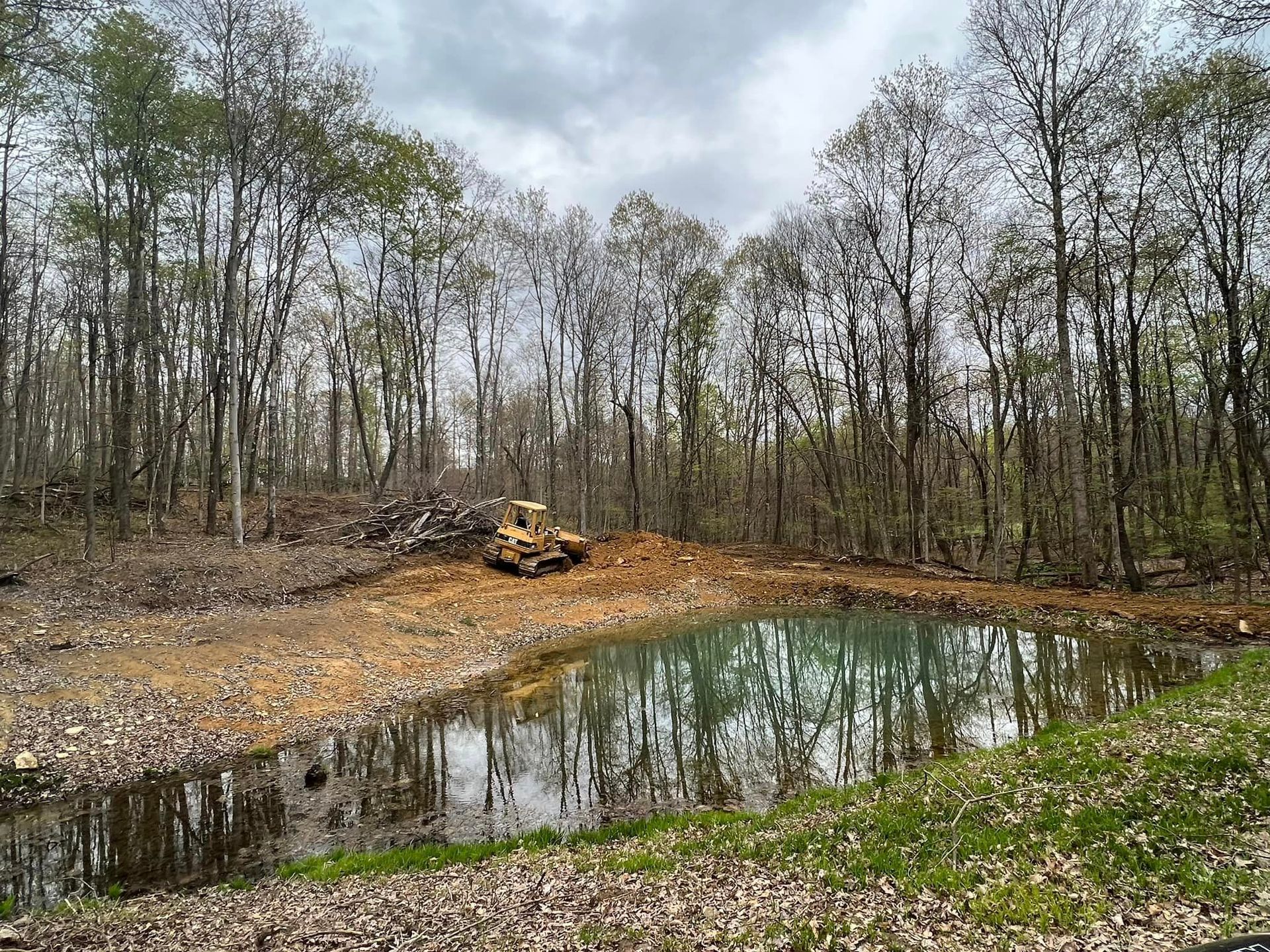 A small pond in the middle of a forest with a bulldozer in the background.