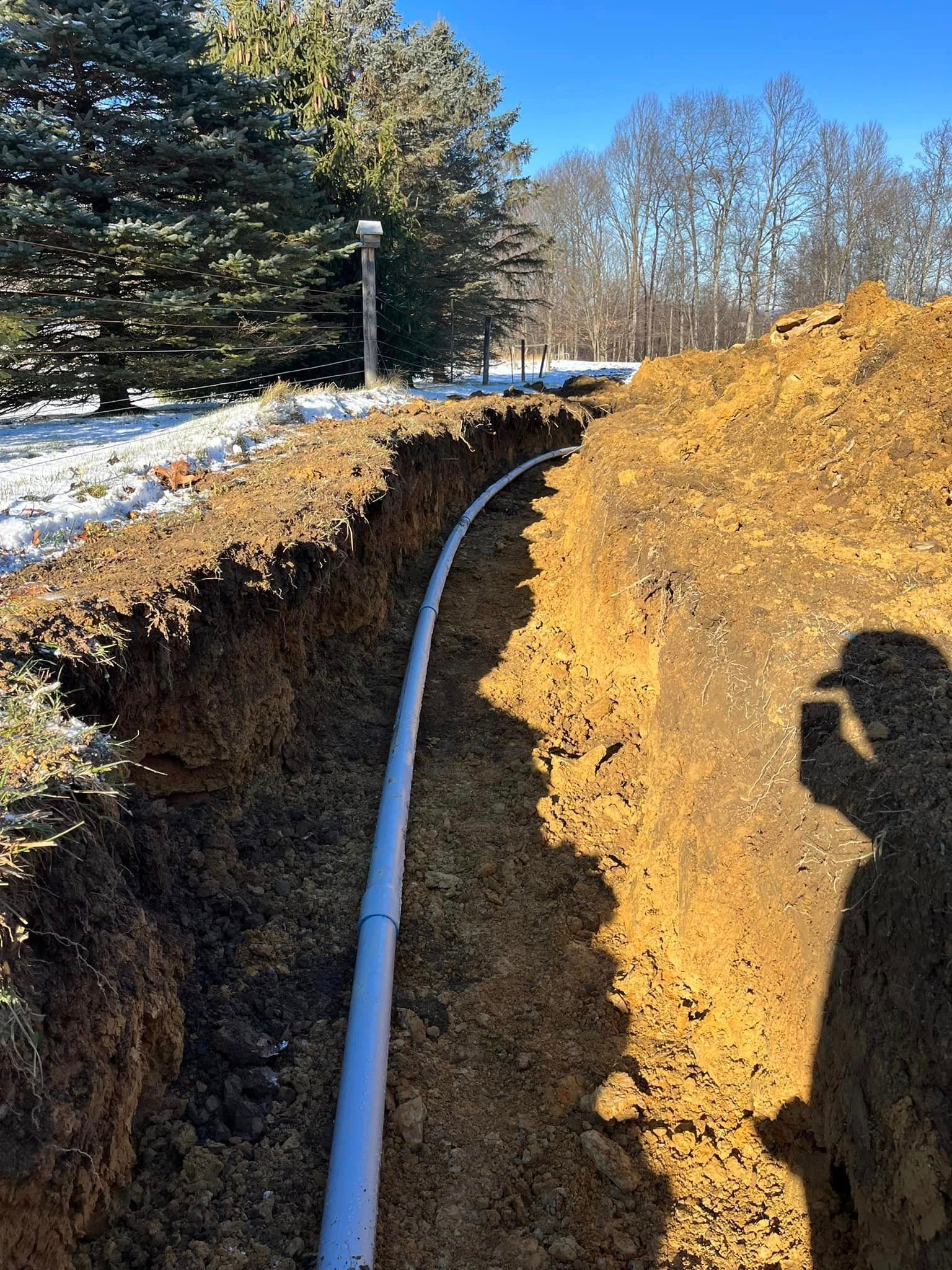 A white pipe is being installed in a trench in the dirt.