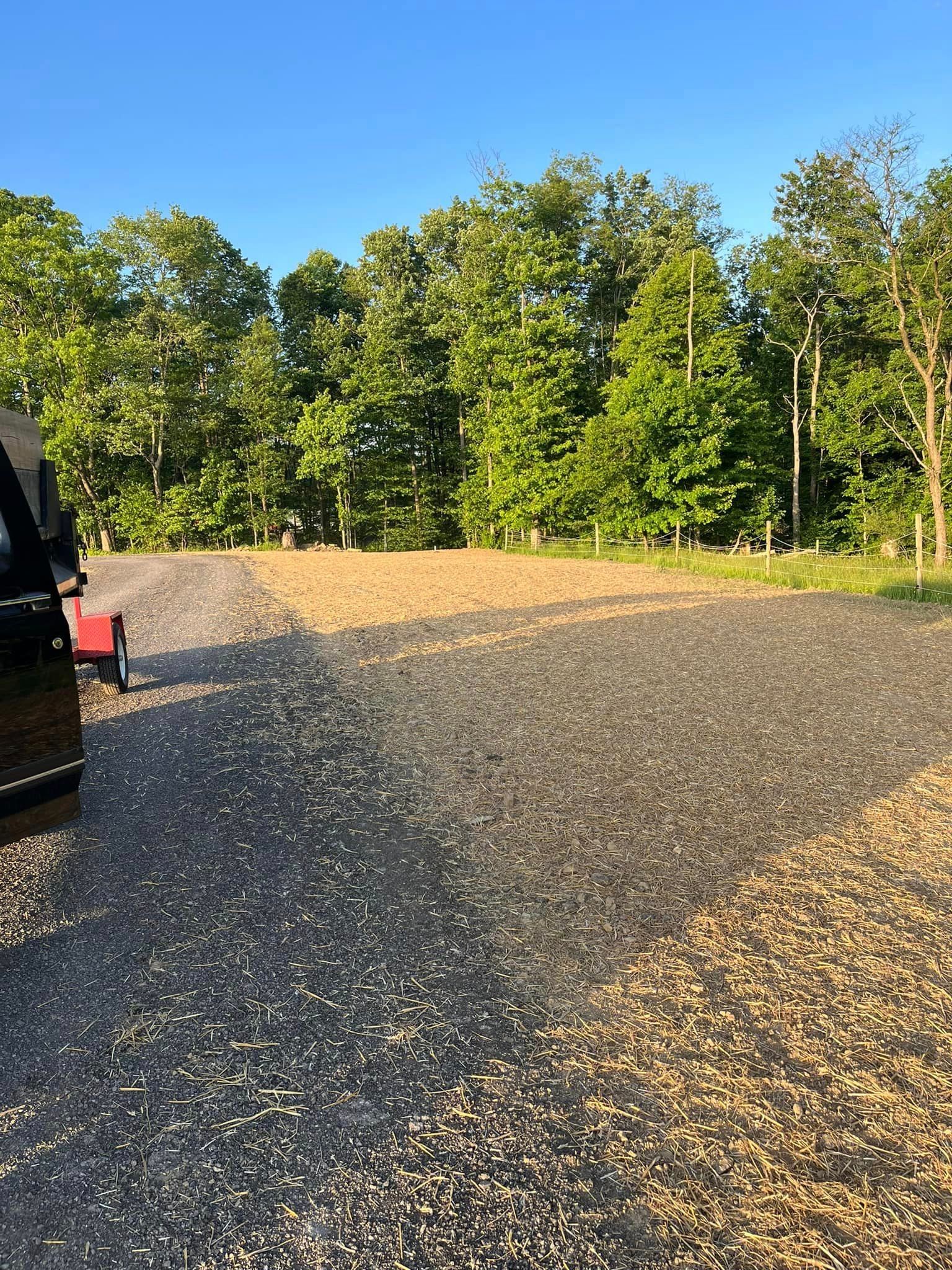 A car is parked in a gravel lot with trees in the background.