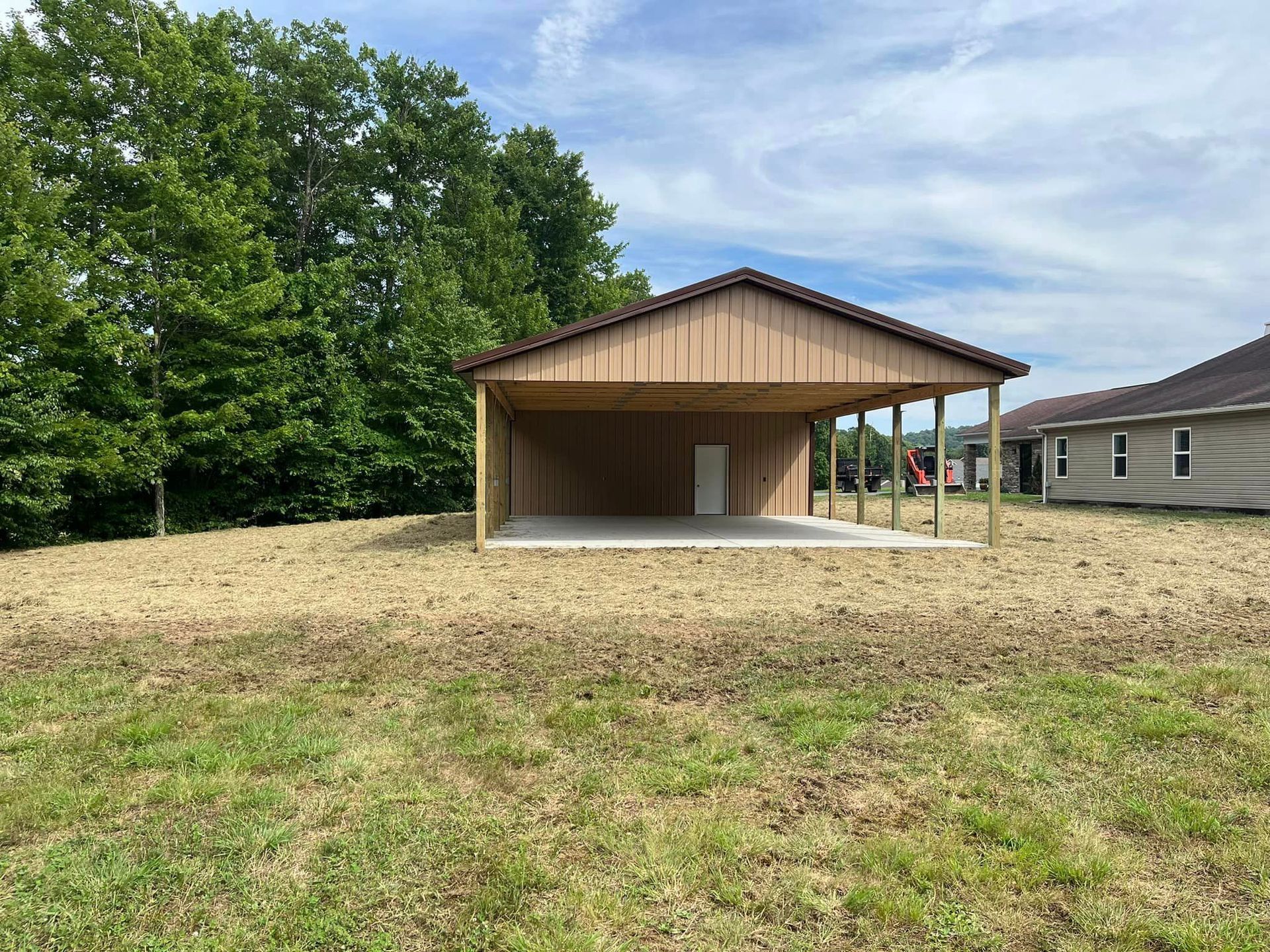 A large wooden garage is sitting in the middle of a grassy field.
