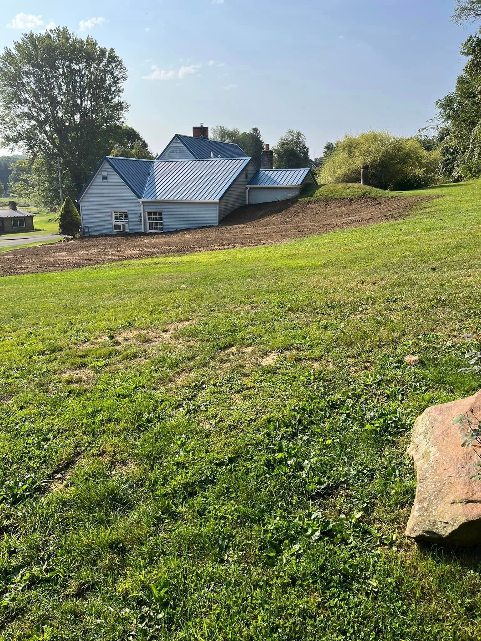 A house with a blue roof is sitting in the middle of a grassy field.