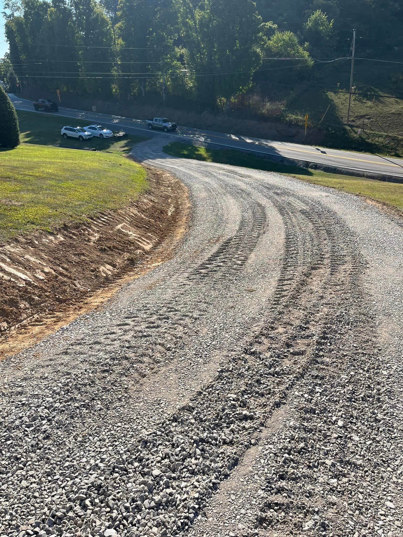 A gravel road going through a grassy area with trees in the background.