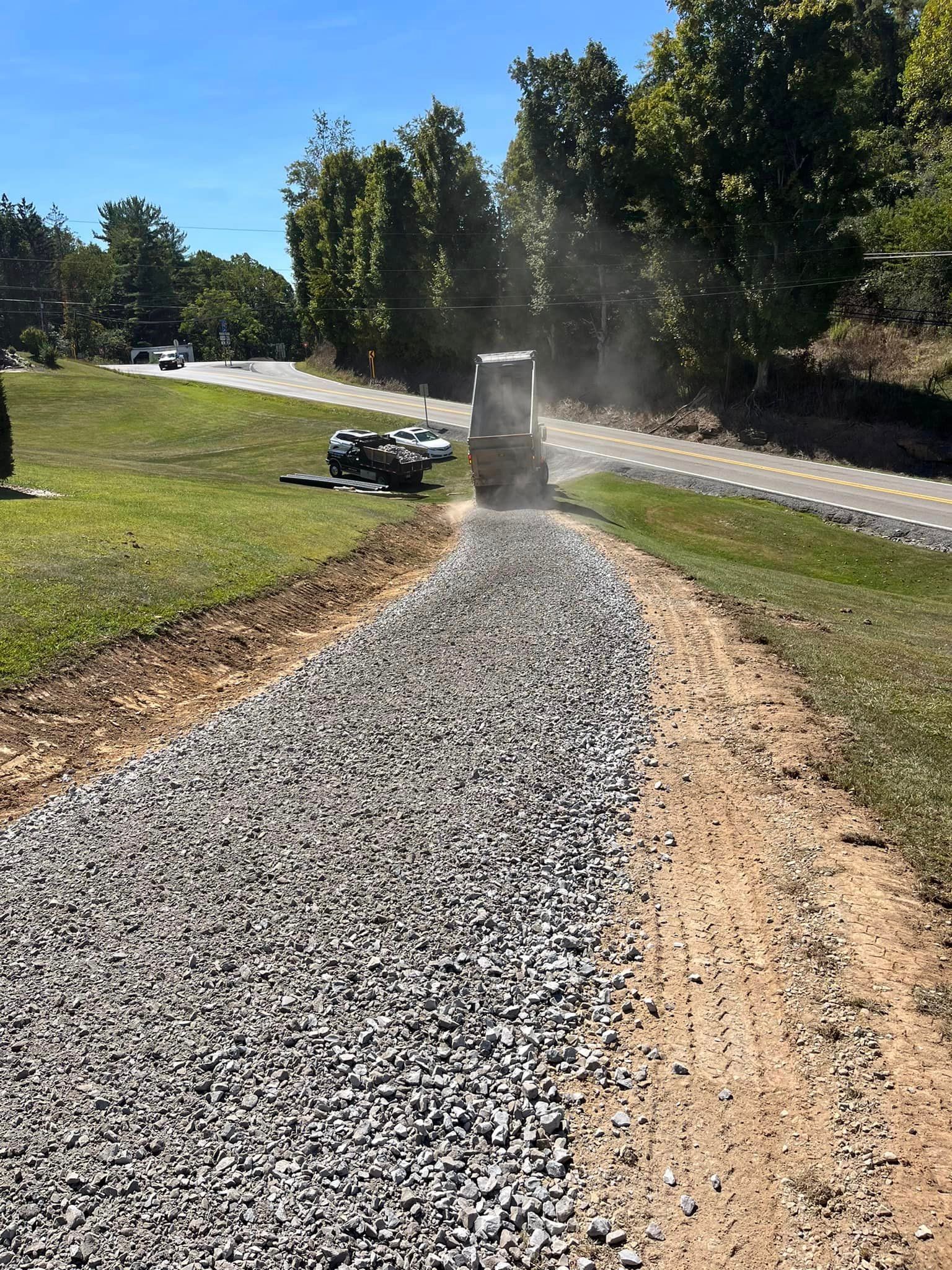 A truck is driving down a gravel road next to a grassy field.
