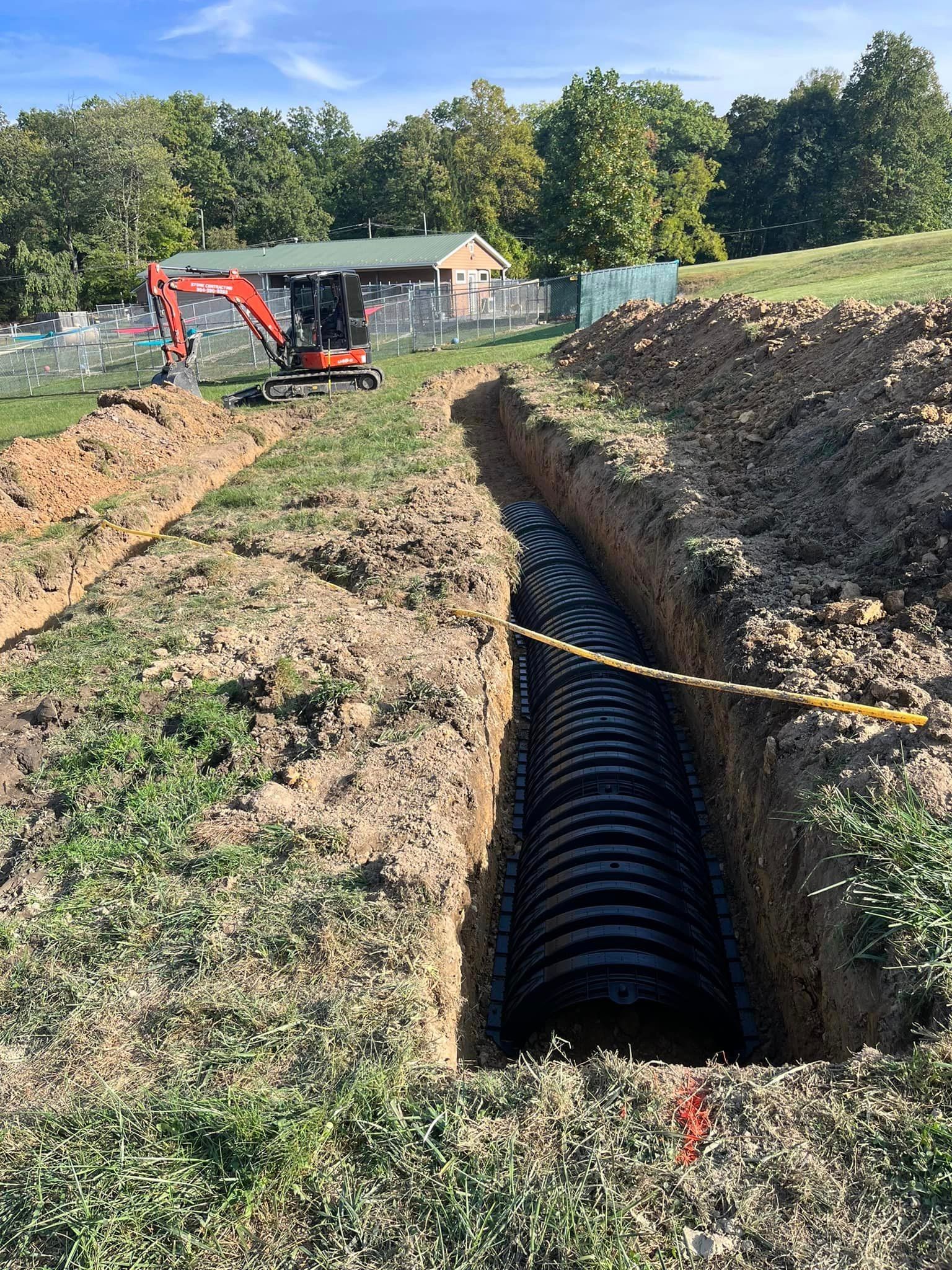A large pipe is being installed in a trench in a field.