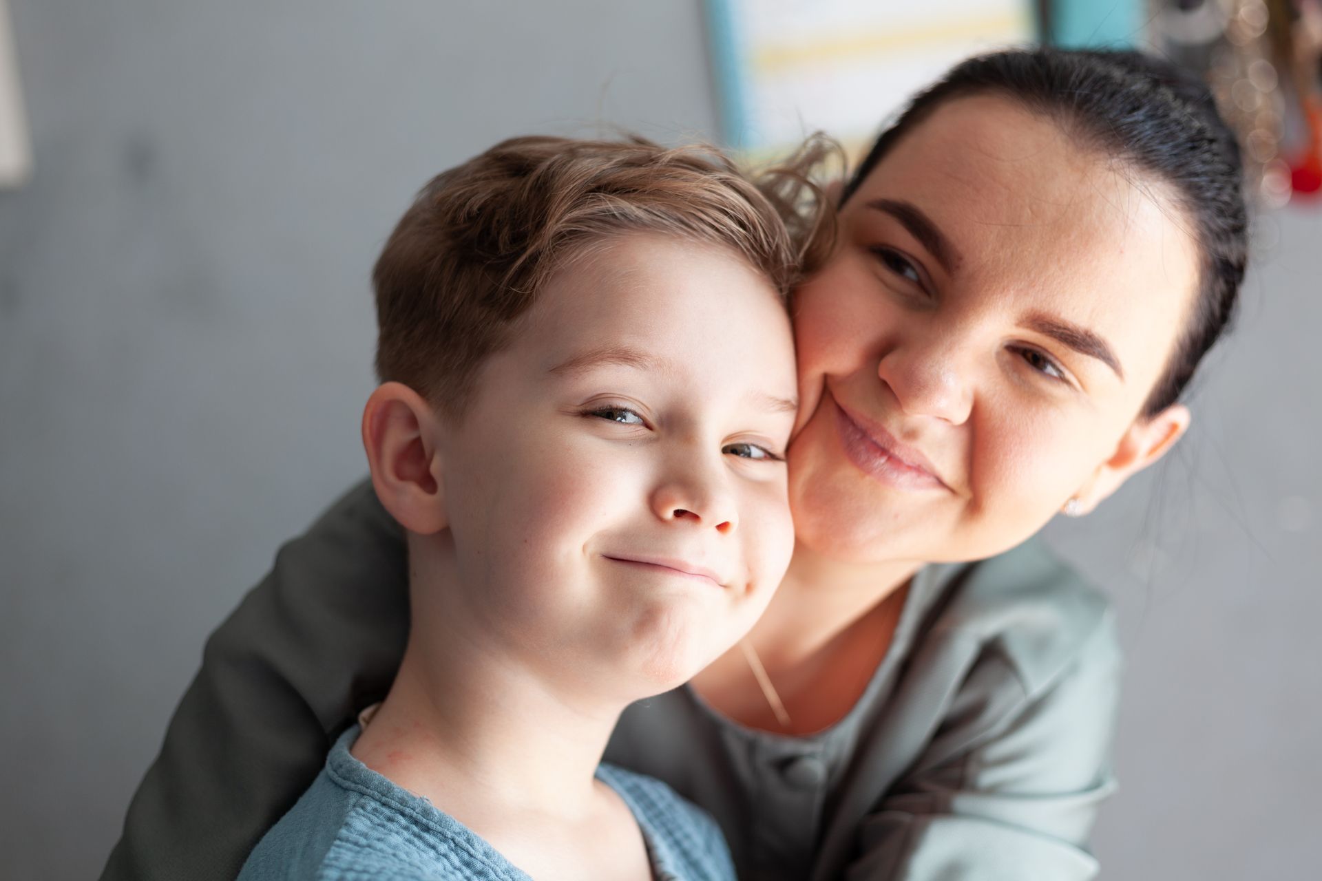 A woman is hugging a young boy who is smiling for the camera.