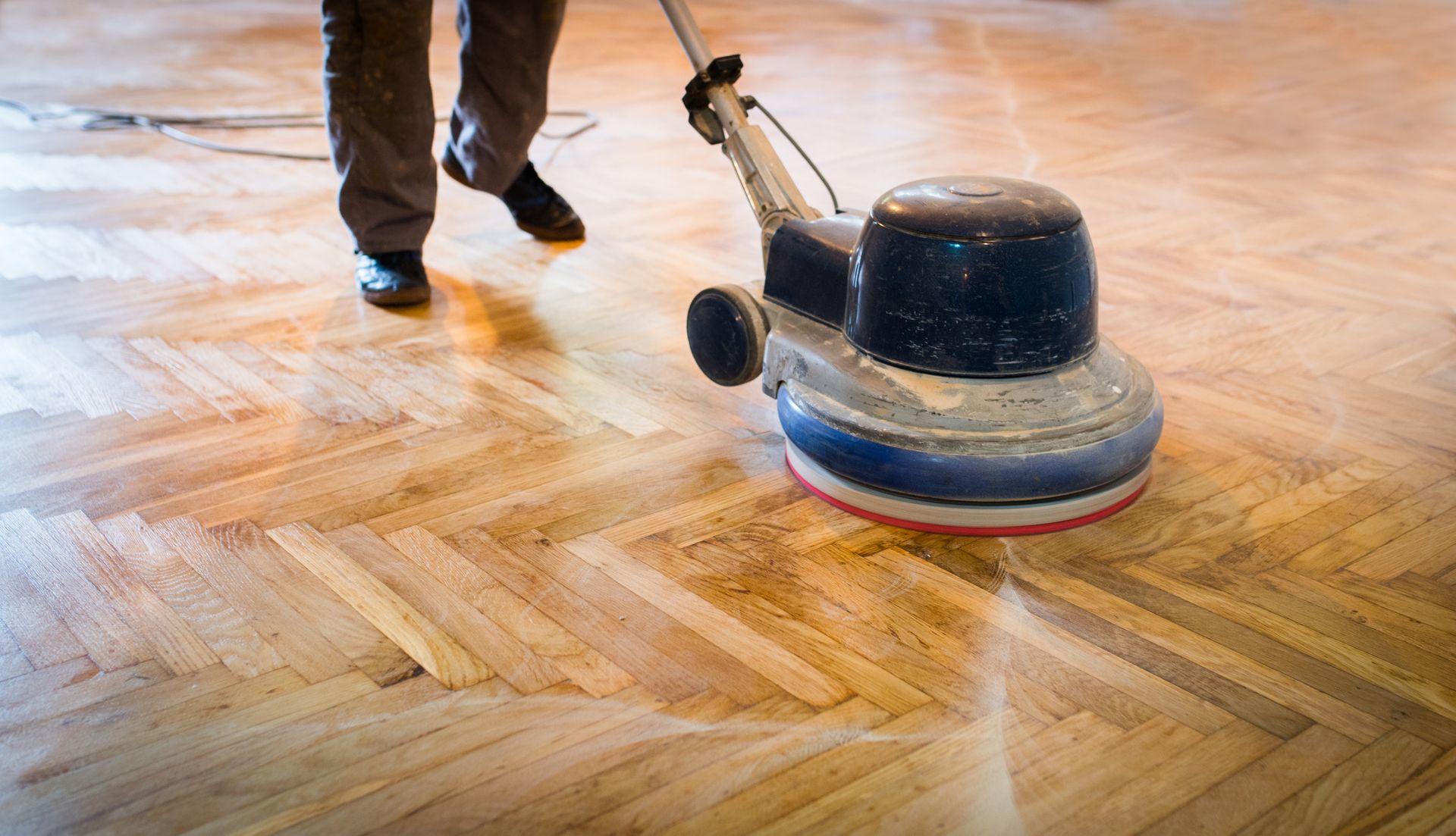 A man operating a floor polisher on a wooden floor, highlighting hardwood flooring sanding.